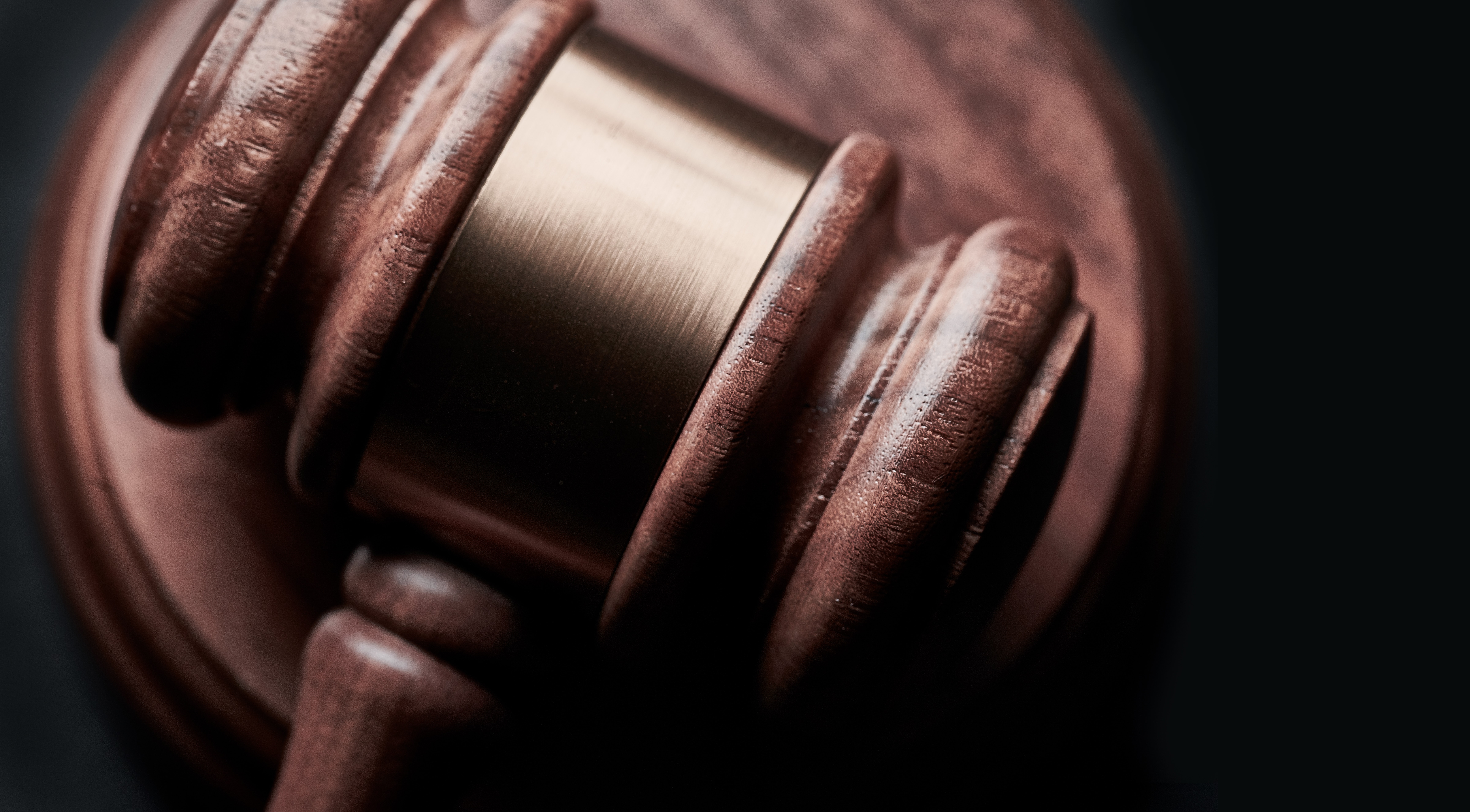 A closeup of a wooden gavel with golden metal band across its head resting on a platform.