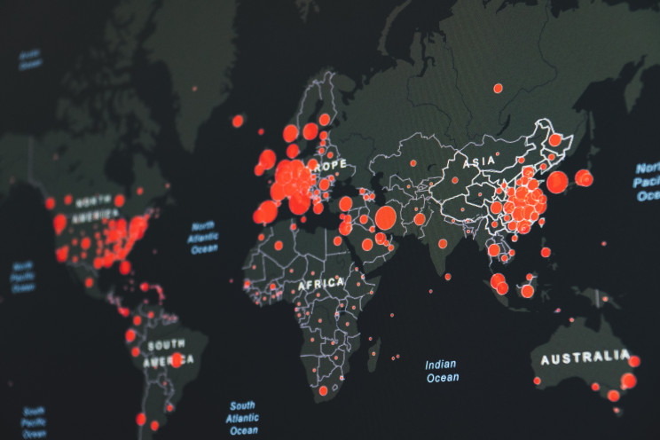A digital map with red circles indicating the prevalence of COVID-19 rates around the world.