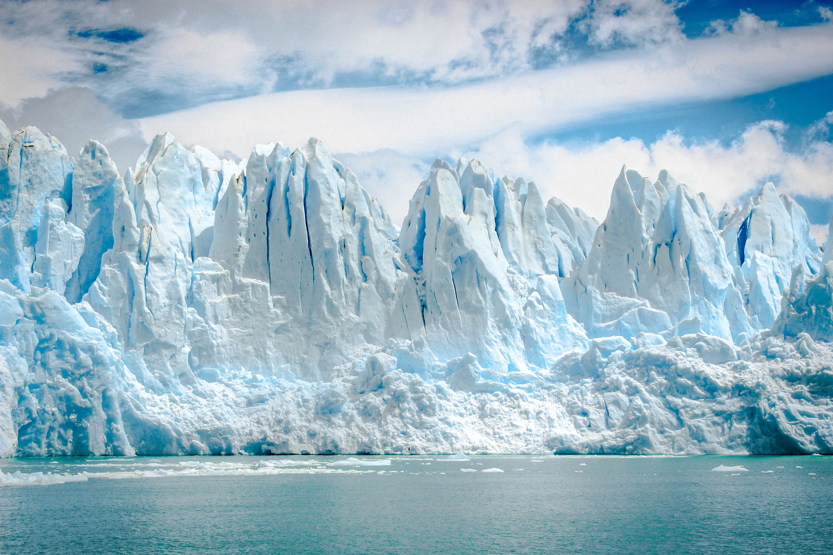 A massive, jagged, deep blue and bright white iceberg sits next to the ocean