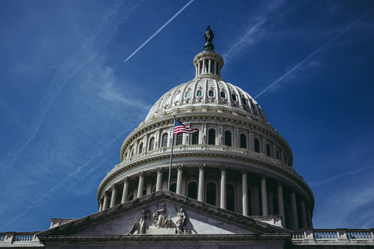 The dome of Capitol Hill in Washington DC against a dark blue sky striped with clouds and jet trails.