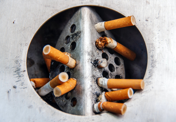 Ten put-out cigarettes line a public cigarette disposal can.