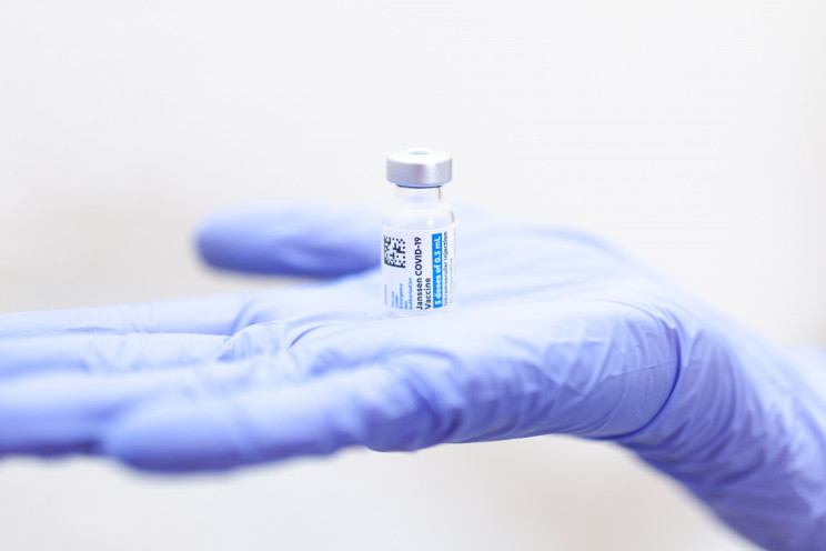 A doctor's hand in a glove holds a vial of the Johnson and Johnson COVID vaccine.